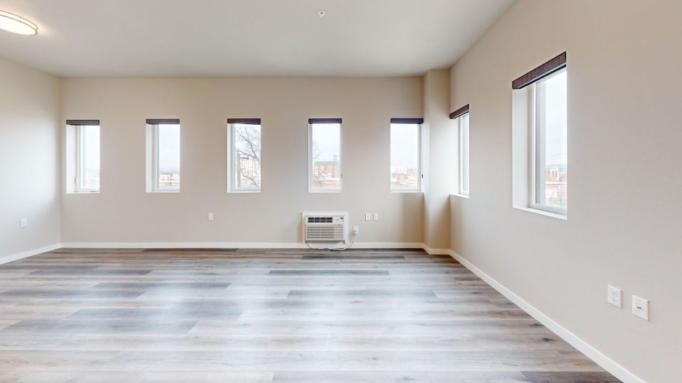Bright living room with laminate floors, light tan walls, and seven windows with built in shades.