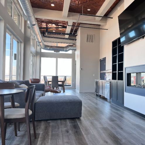 View of 508 West's modern penthouse for entertaining. Tall ceilings feature white pillars, copper ceiling, wood cabinets and white counters, and dark blue entertainment center with TV, modern couches and views of Spokane.