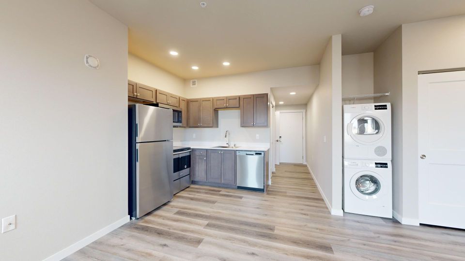 Open concept kitchen and living room with recessed lighting, walnut cabinets, stainless steel appliances and stacked washer dryer next to a closet.