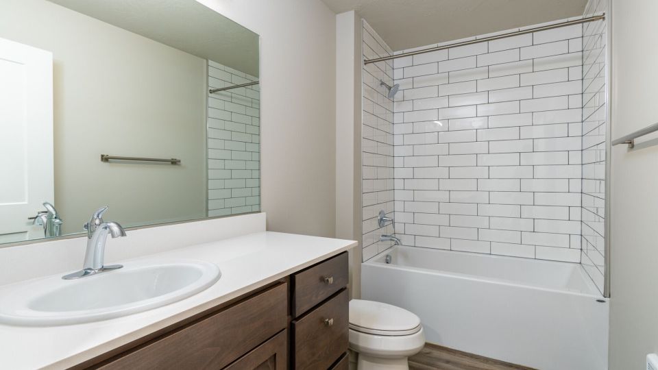 Large bathroom with walnut vanity, white countertop, and bath shower combo with white subway tile.