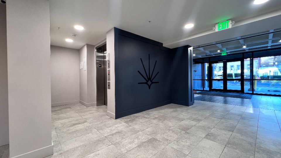 View of art deco style lobby elevator area with dark blue paint, bright light, wood panel accents, and a view of a conjoining lounge wetbar.