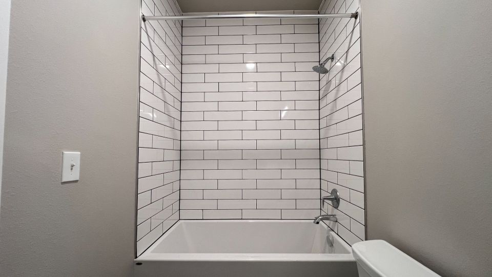 Large bathroom with white countertops, white subway tiles, shower and tub combo, walnut colored cabinet, and stacked washer dryer.