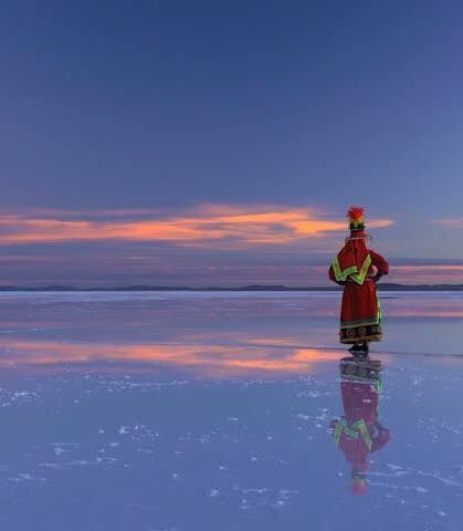 Person in traditional dress on a reflective salar at dusk