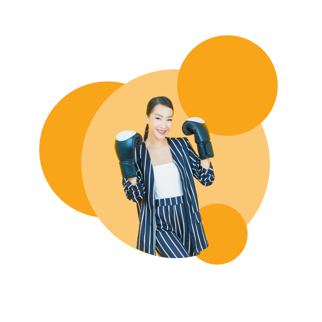 Asian woman in a navy suit with white stripes, with black and white boxing gloves one looking ready to box, while smiling.