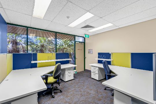 Image of medium sized office with a large window and emergency exit door. Two large corner desks in either corner of the room.