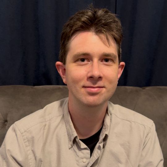 Portrait of Sebastian H, smiling and friendly against a dark background.