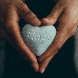 Close up of hands holding a heart shaped stone that says, hope