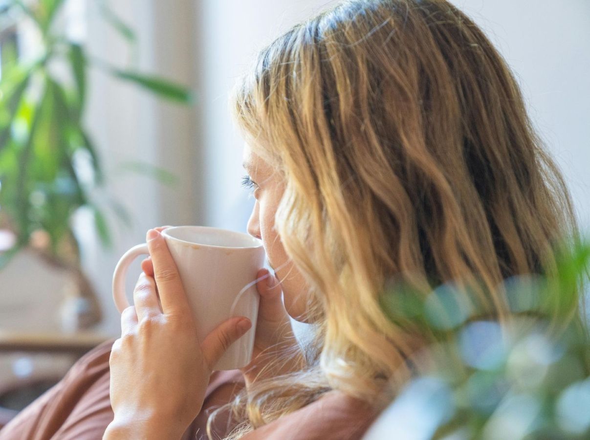 Woman quietly sipping a cup of tea curled up peacefully looking out the window.