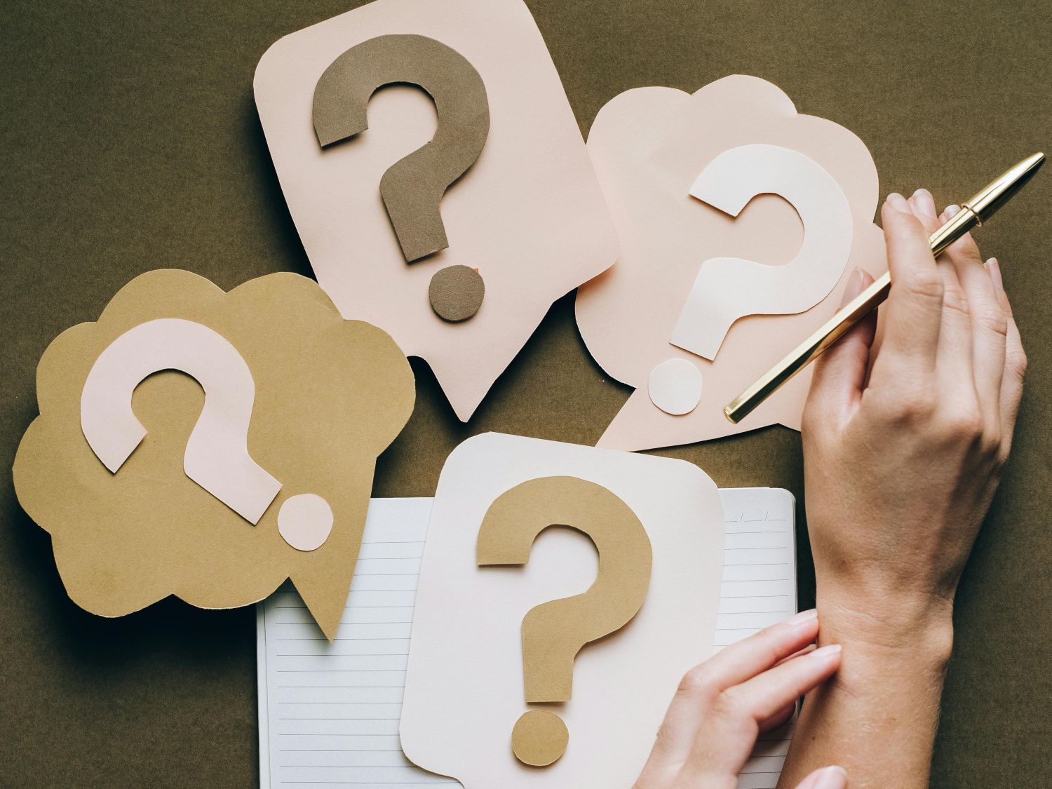 Soft brown and beige question marks cut from paper and a hand reaching calmly for one.