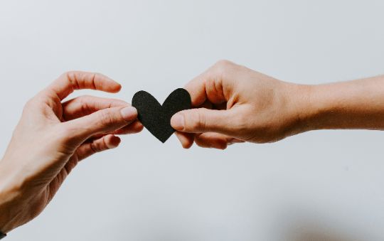 close up of two hands holding a paper heart between them