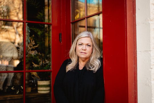 Portrait of Amy K smiling, standing in a large doorway, outside