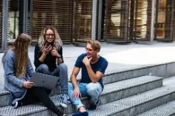 Students sitting happily together outside on the steps of college classroom.