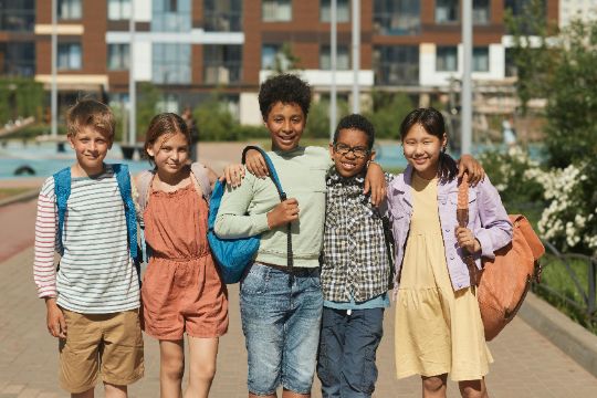 Group of younger students posing with arms around each other and their backpacks, happy and excited to start school.