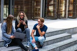Students sitting happily together outside on the steps of college classroom.
