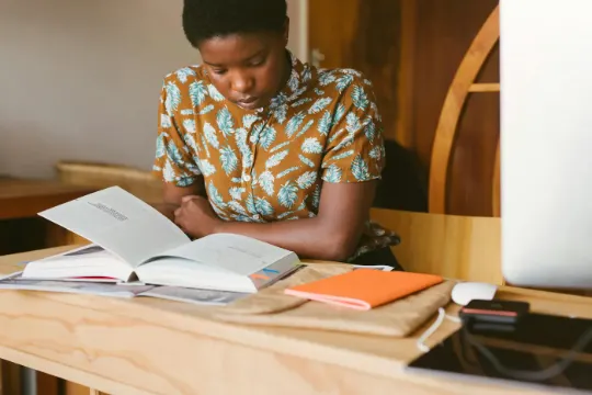 Student sitting at a desk reading a text book with their computer, studying.