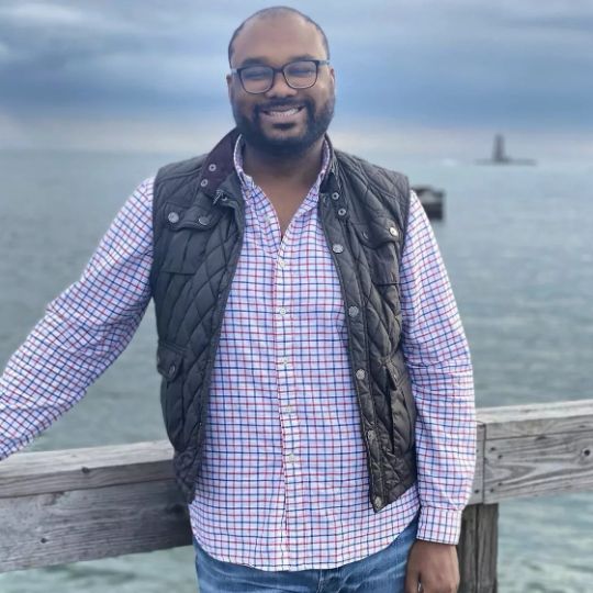Portrait of John R standing outside at an ocean pier, smiling and friendly