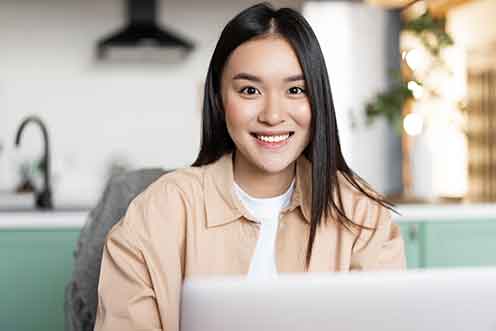 freelance-asian-girl-sitting-home-working-with-laptop-smiling-camera-young-woman-using-com